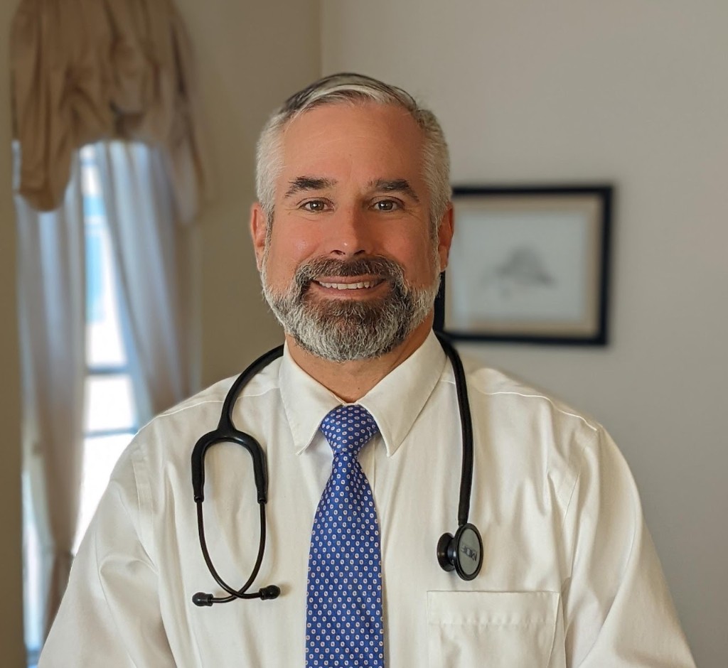 Philip A. Huffman, MD, in a white shirt and blue tie with a stethoscope